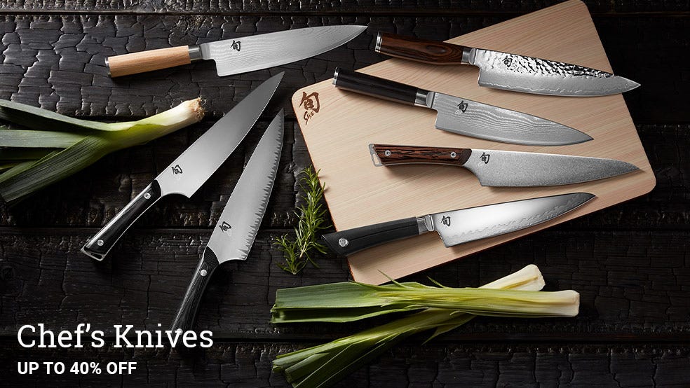 A grouping of Shun Chef's Knives lying on a table around a Hinoki cutting board.