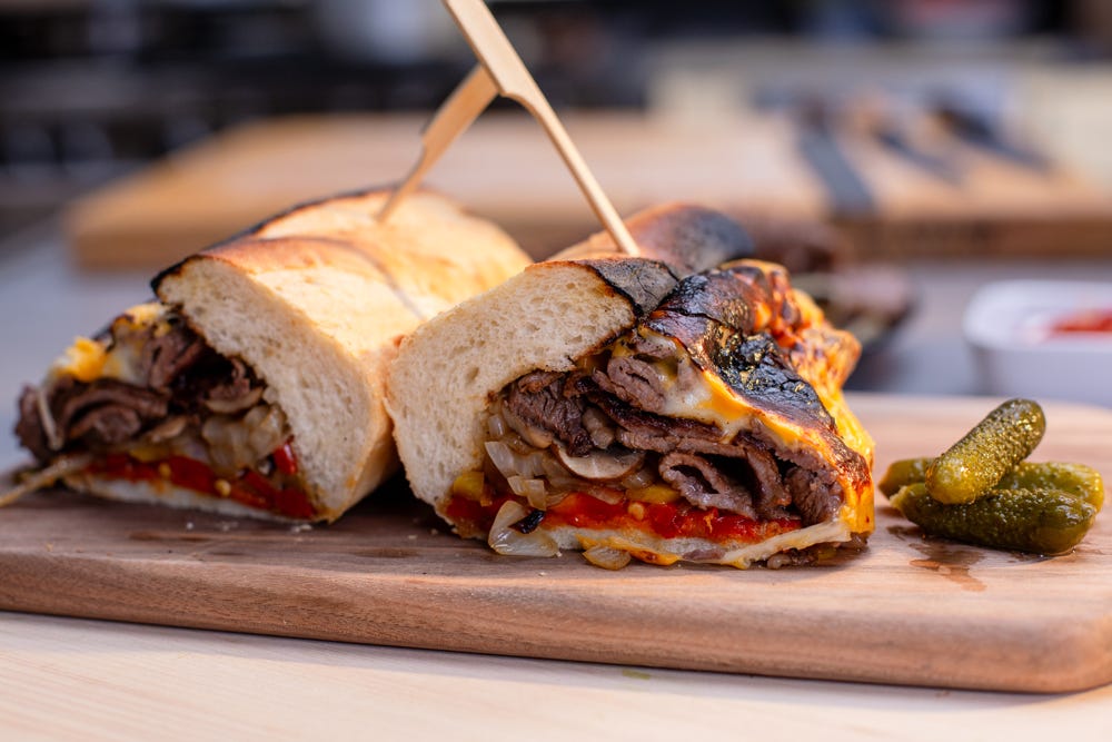 A Ribeye Cheesesteak sandwich sliced in half, resting on a serving platter.