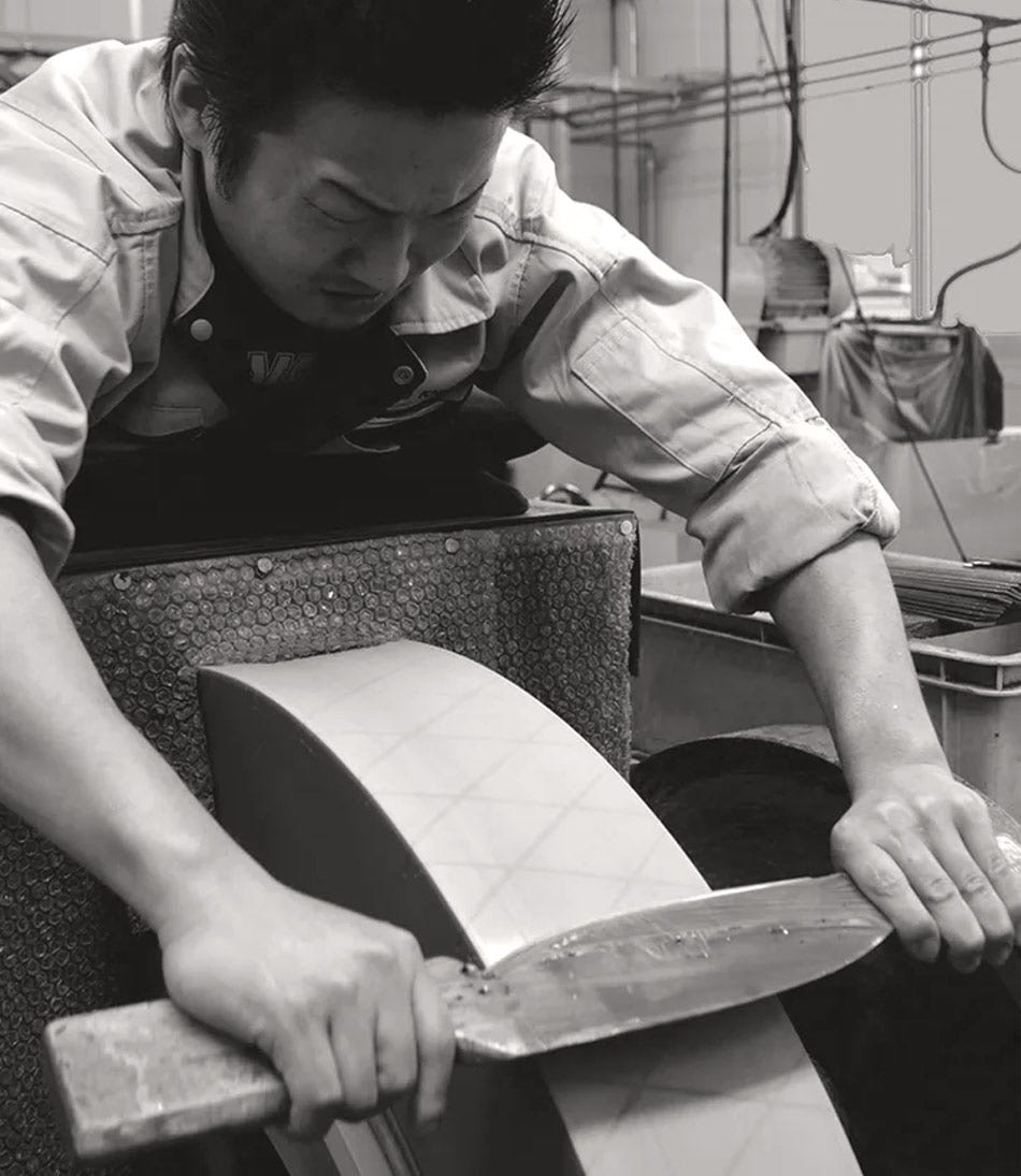 Black-and-white image of a craftsman sharpening a knife in Japan.