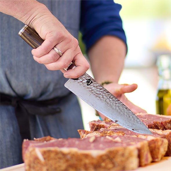 Chef’s knife in use slicing cooked meat on a cutting board.