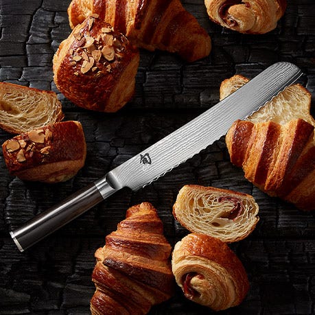Shun Classic bread knife styled with pastries on a dark textured surface.