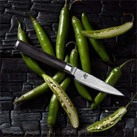 Shun Classic paring knife styled with green chiles on a dark textured surface.