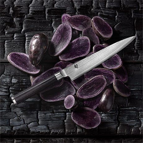 Shun Classic utility knife styled with purple potatoes on a dark textured surface.