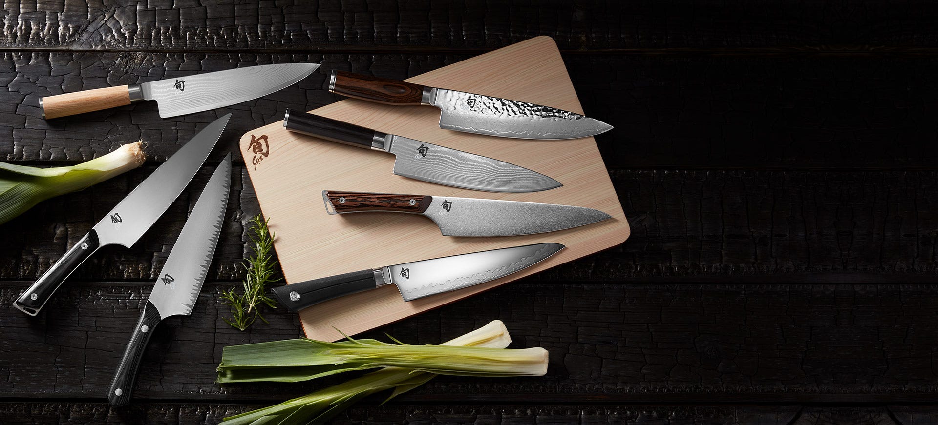 Selection of Shun knives from different series arranged on cutting boards over a dark wood surface.