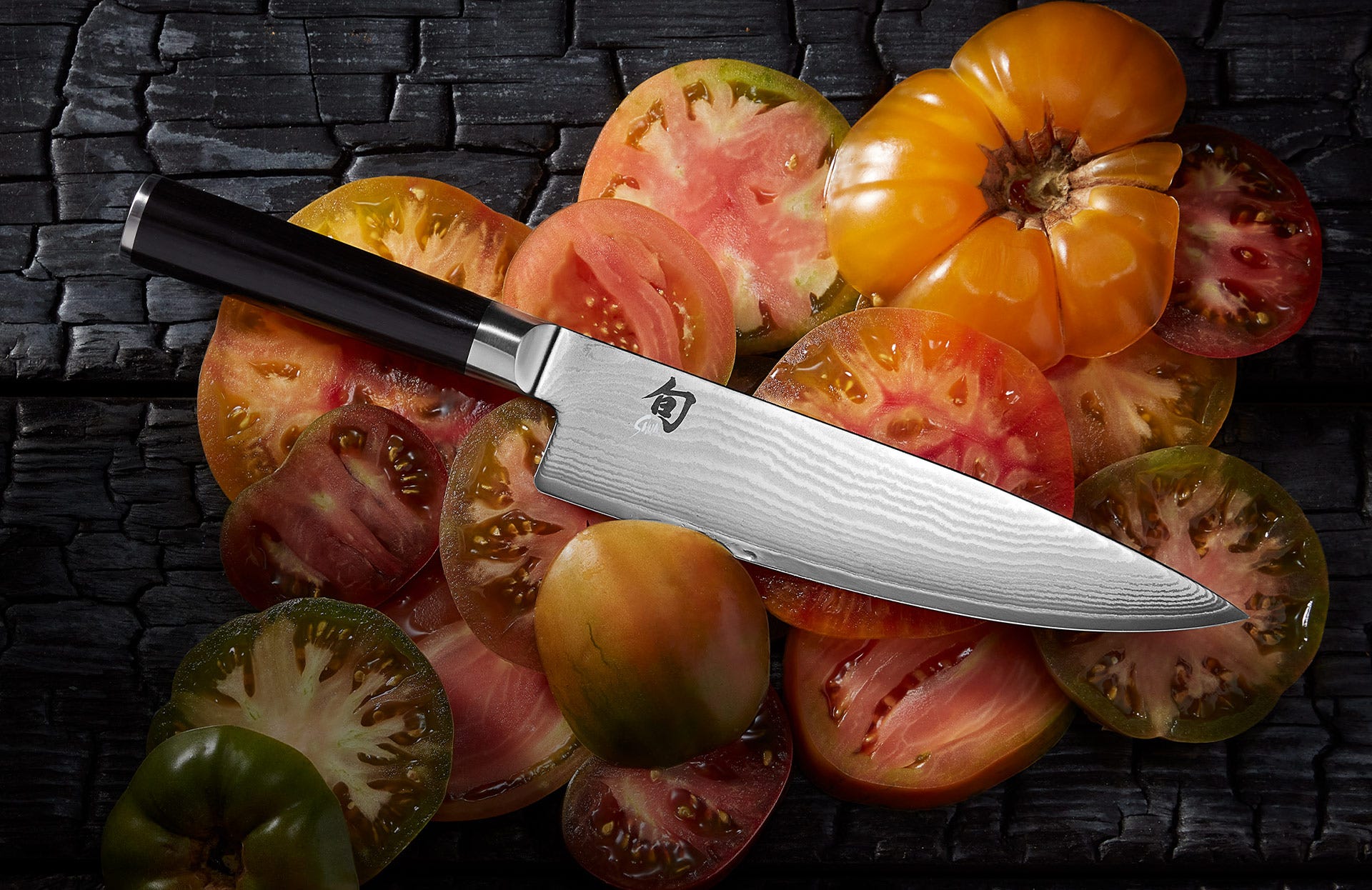 Shun Classic chef’s knife on sliced heirloom tomatoes over a dark wood surface.