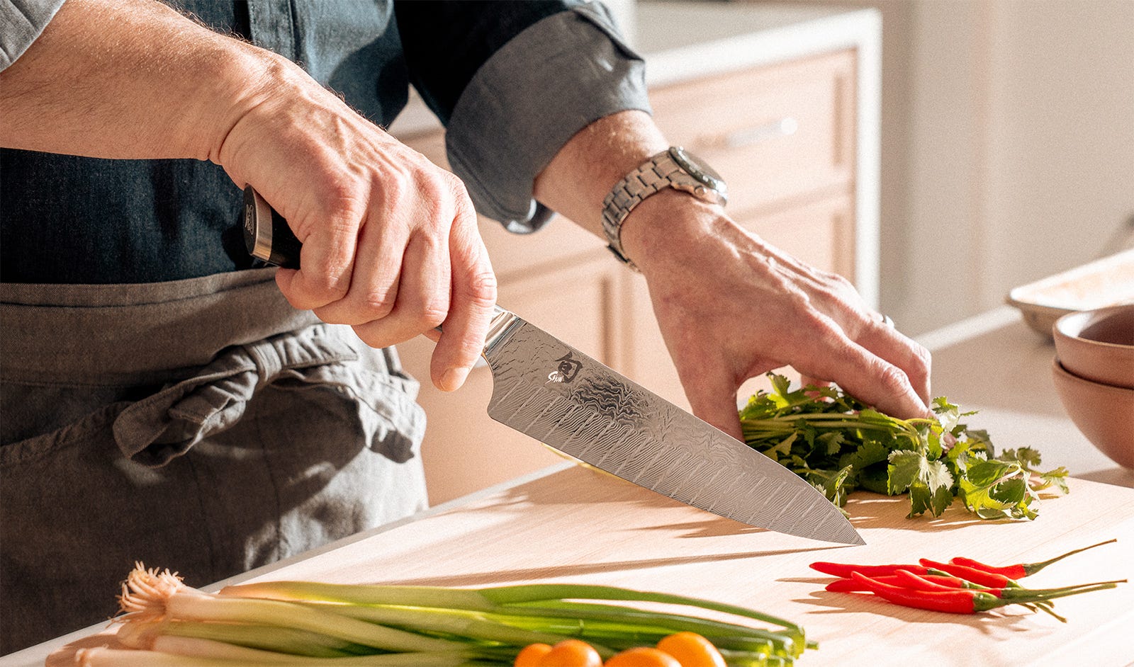 Chef slicing fresh herbs with a Shun Shiranami chef’s knife on a wooden cutting board