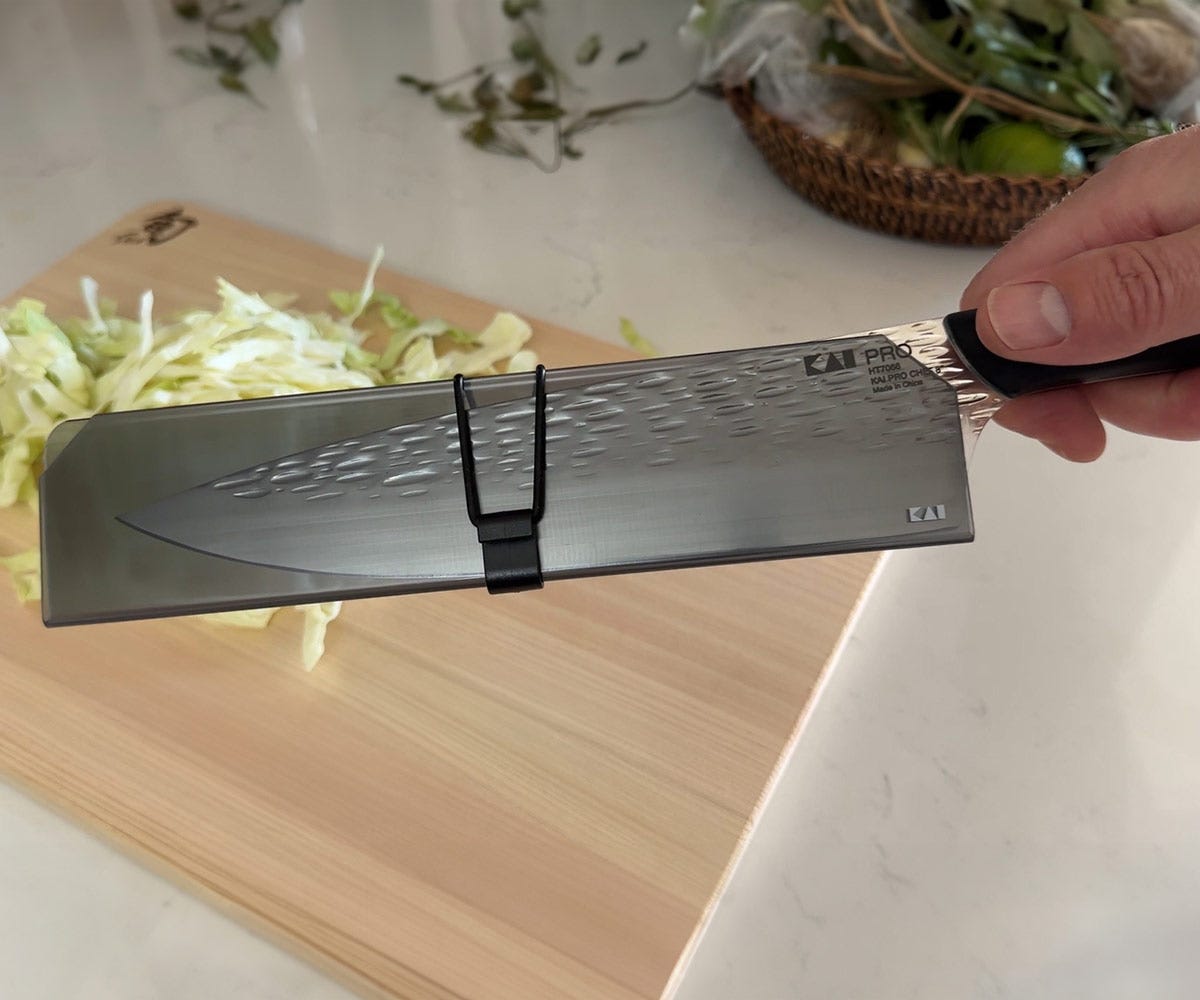 Shun knife protected with a blade guard in front of a Hinoki cutting board, demonstrating safe storage and edge protection.