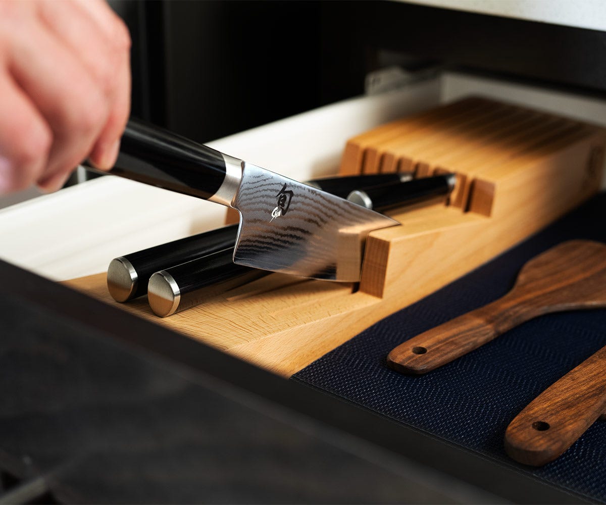 Shun knife being placed spine-first into an in-drawer wooden knife tray, showing proper knife storage to protect the blade.