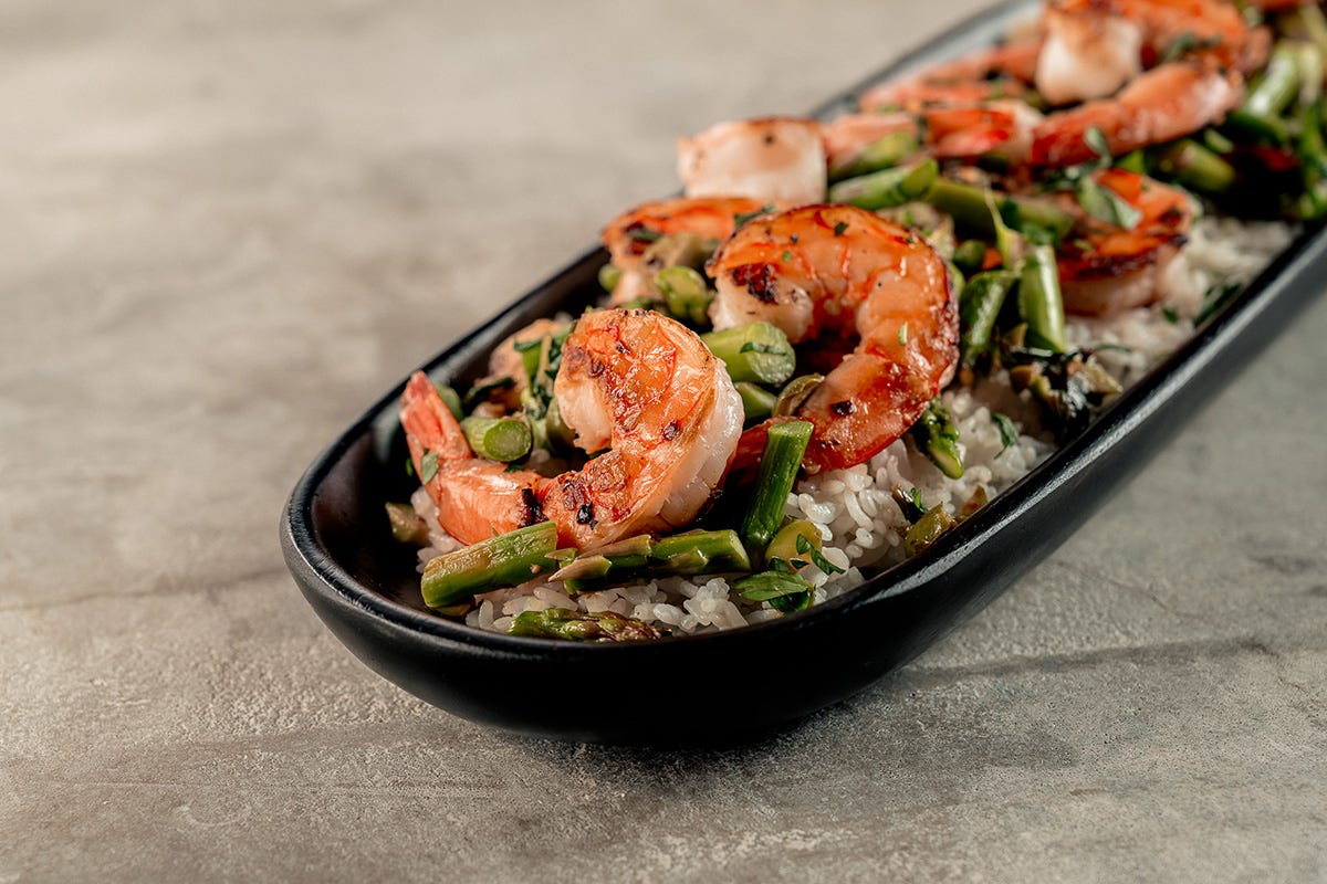 Close up of Bill Kim's garlic shrimp with asparagus, plated on a oval, ceramic stoneware plate.
